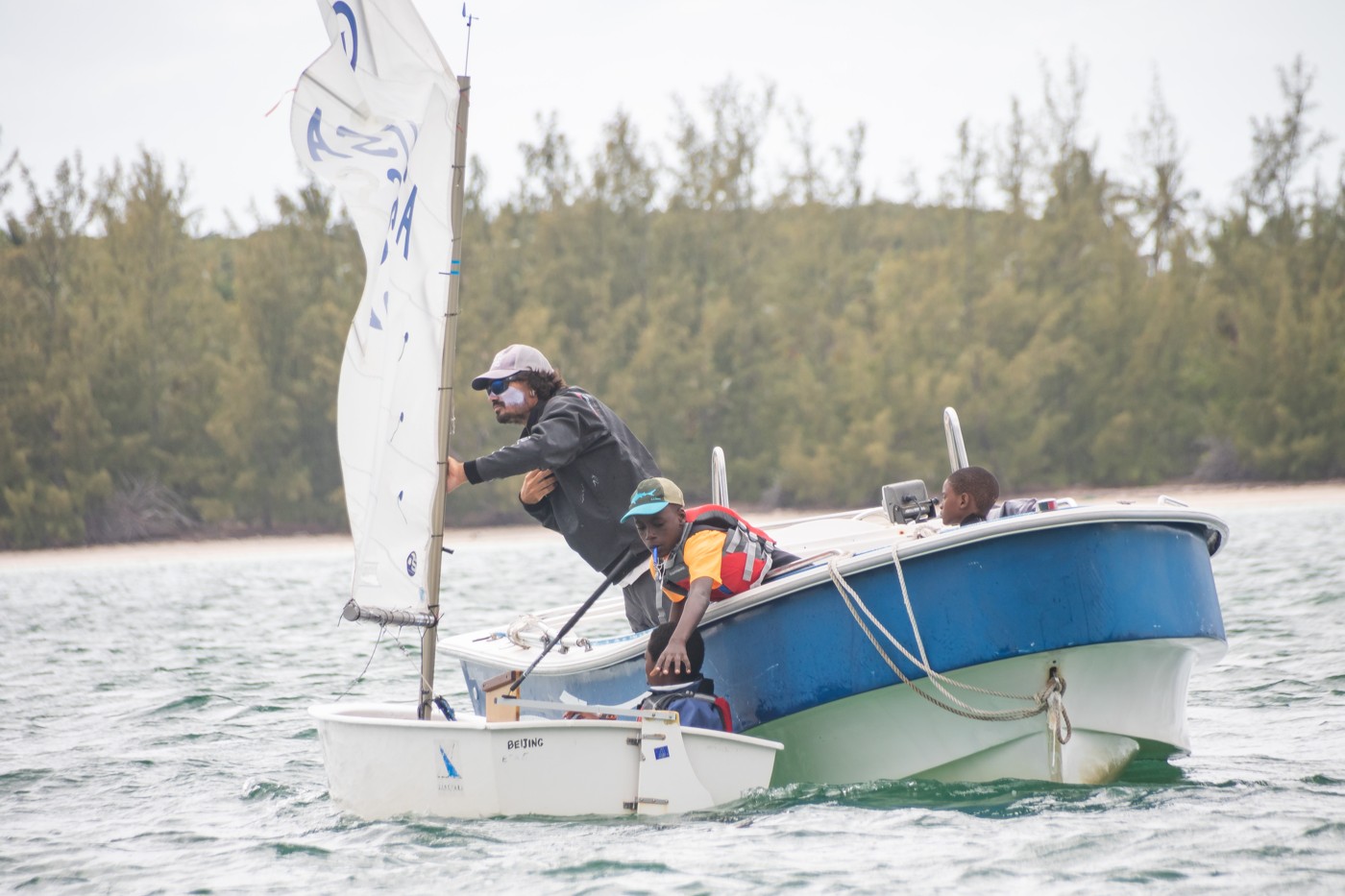 ESA coach guiding a young Optimist sailor on the water
